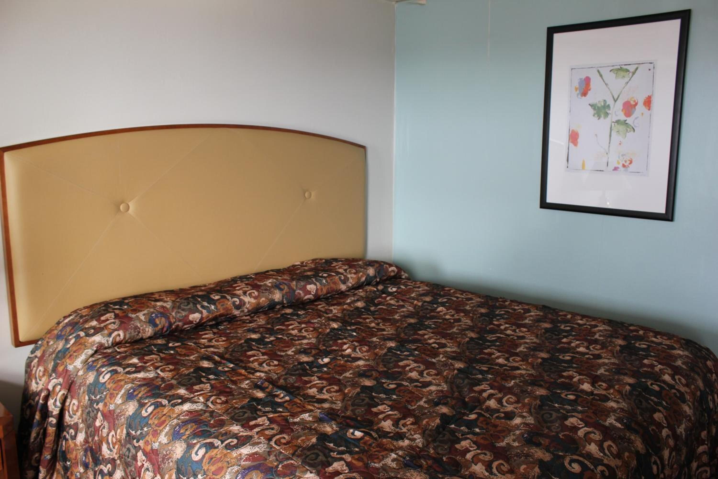 Uma cama com colcha estampada, cabeceira e quadro pendurado na parede.