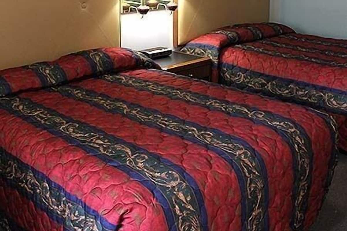 Une chambre d’hôtel avec deux lits, chacun recouvert d’une couvre-lit à motifs rouges et bleus, une table de chevet avec une lampe et un luminaire fixé au mur.