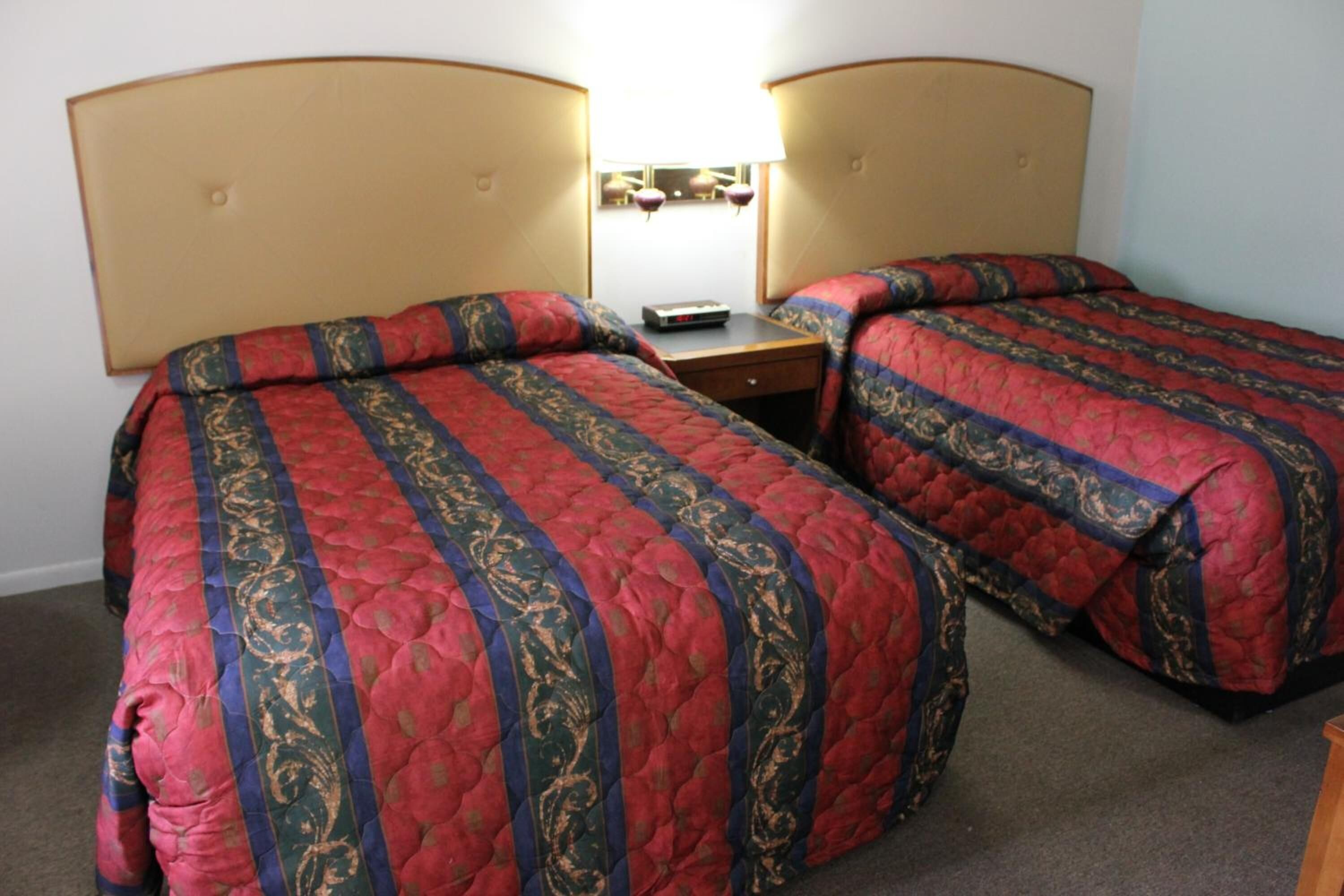 A hotel room with two single beds, each with a headboard, a bedside table, and a lamp.