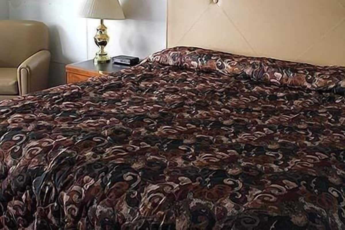 Une chambre d’hôtel avec un lit, une chaise, une lampe et une petite table.
