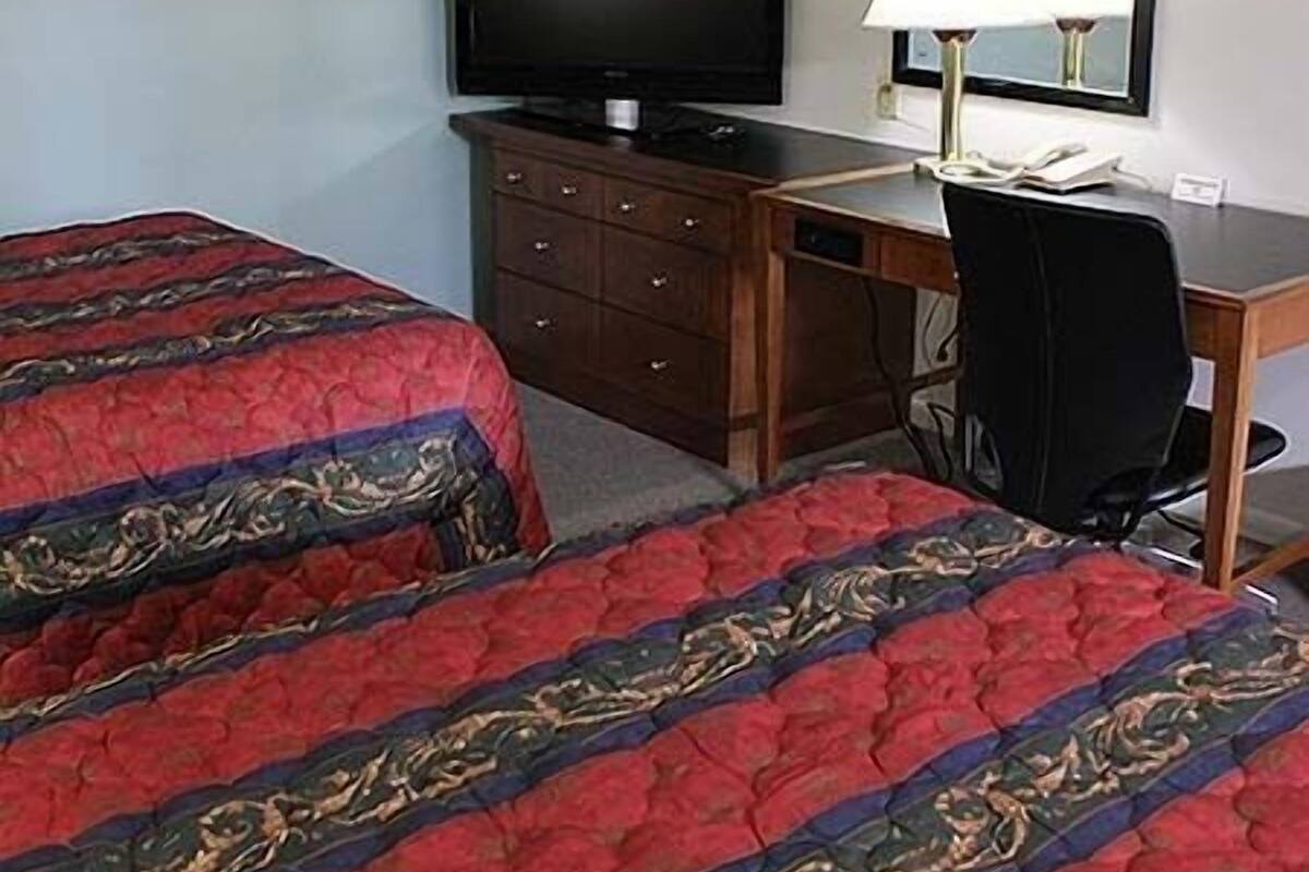 Une chambre d’hôtel avec deux lits, un bureau, une chaise, une télévision et un miroir.