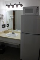 Baño con lavamanos, espejo y un microondas sobre un refrigerador.