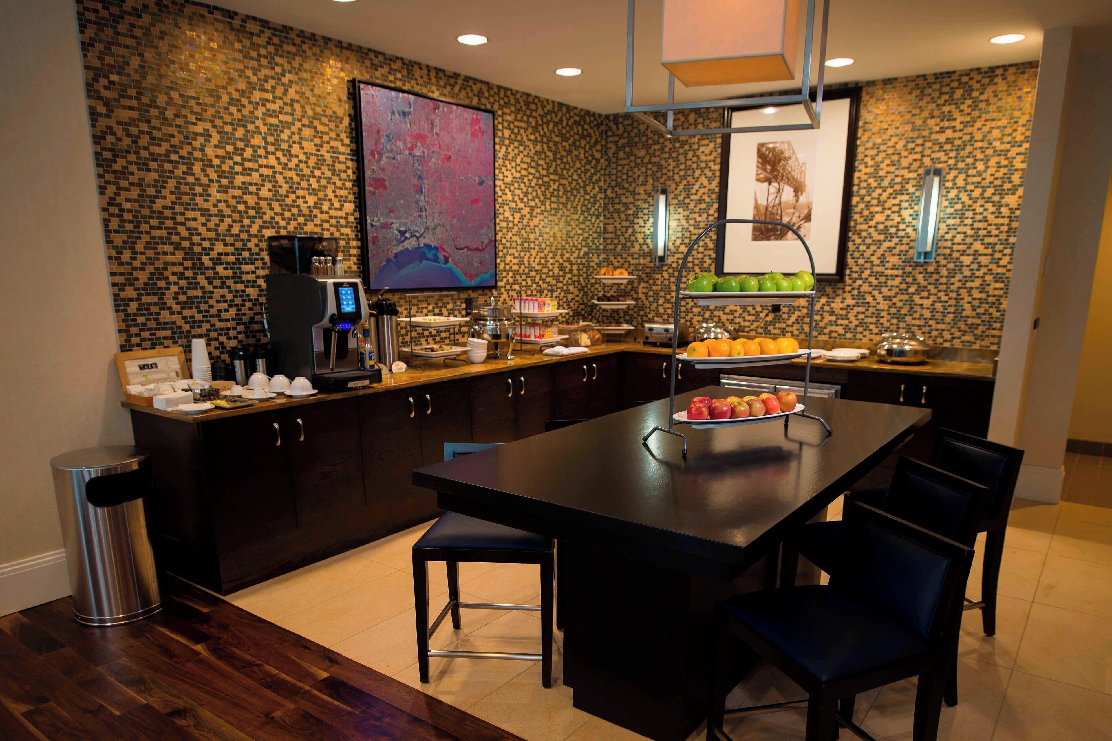 A modern kitchen with dark wood cabinets, a large island with seating, a coffee machine, and a fruit display.