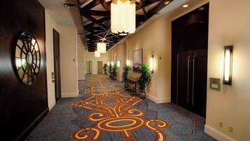 A hotel hallway with patterned carpet, wooden doors, and pendant lighting.