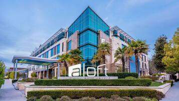 A modern hotel with a prominent glass facade, a covered entrance, and well-maintained landscaping.