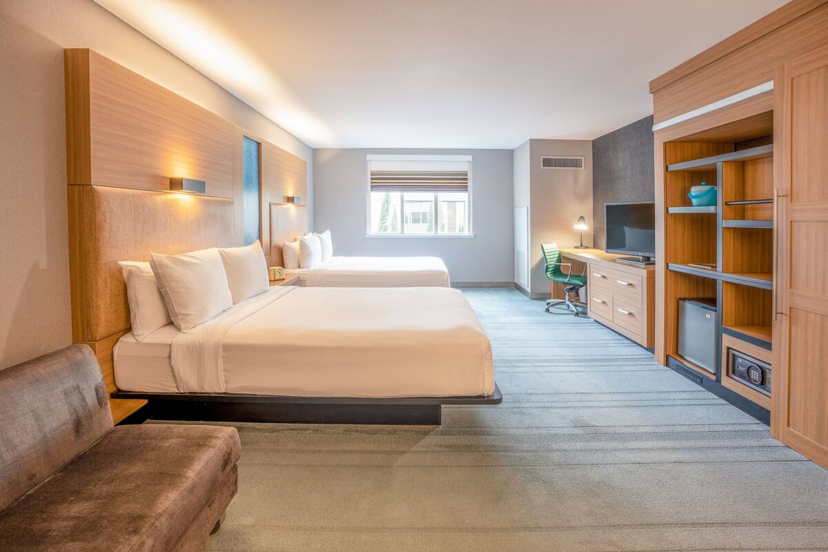 A hotel room with two beds, a sofa, a TV, and a minibar.