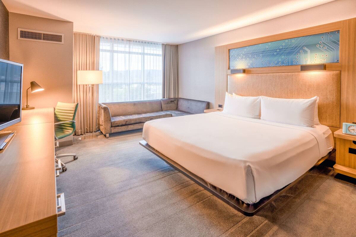 A hotel room with a large bed, a sofa, a desk with a computer, and a TV.