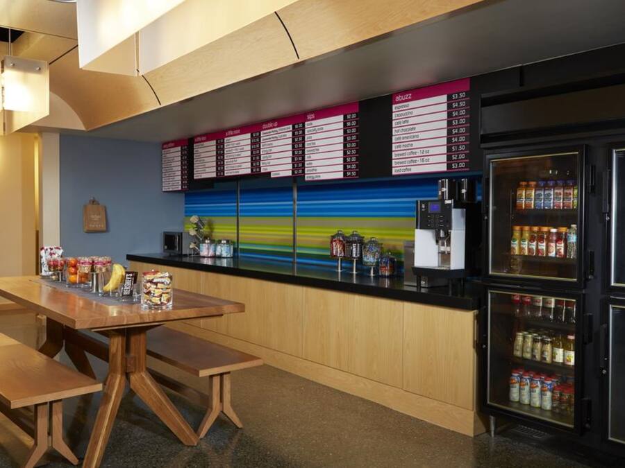 A modern cafe with a wooden counter, a menu board, and a refrigerator stocked with beverages.