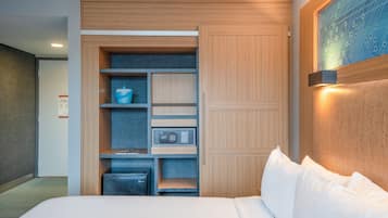 A hotel room with a bed, a built-in wardrobe, a desk with a chair, and a wall-mounted light fixture.