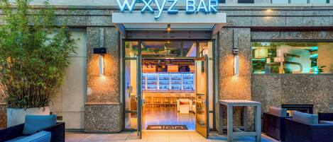 The exterior of WXYZ BAR with a glass entrance, outdoor seating, and a bar area visible inside.