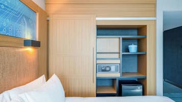 A modern bedroom with a bed, a built-in wardrobe, a small refrigerator, and a wall-mounted artwork.
