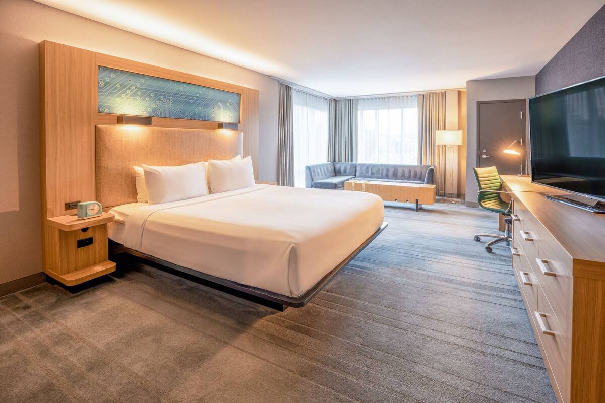 A hotel room with a large bed, a desk with a chair, a television, and a window with curtains.