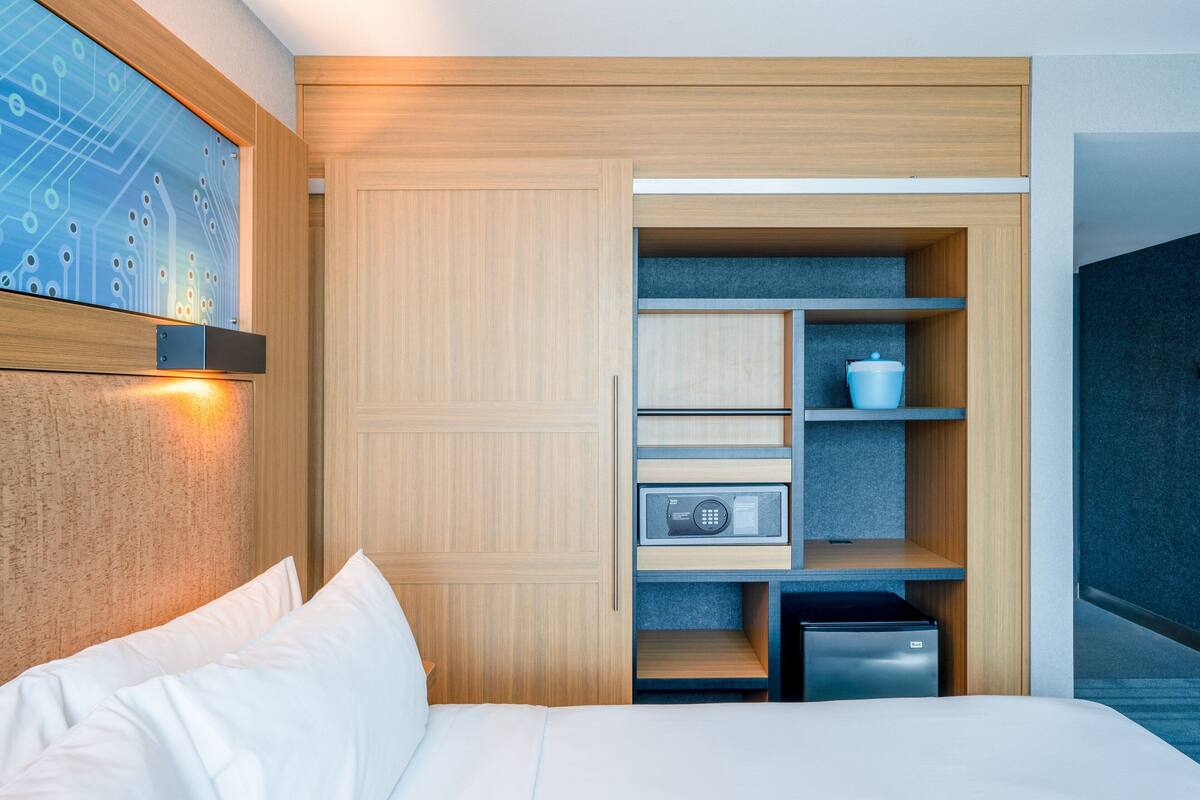 A modern hotel room with a bed, a built-in wardrobe, a microwave, and a small refrigerator.