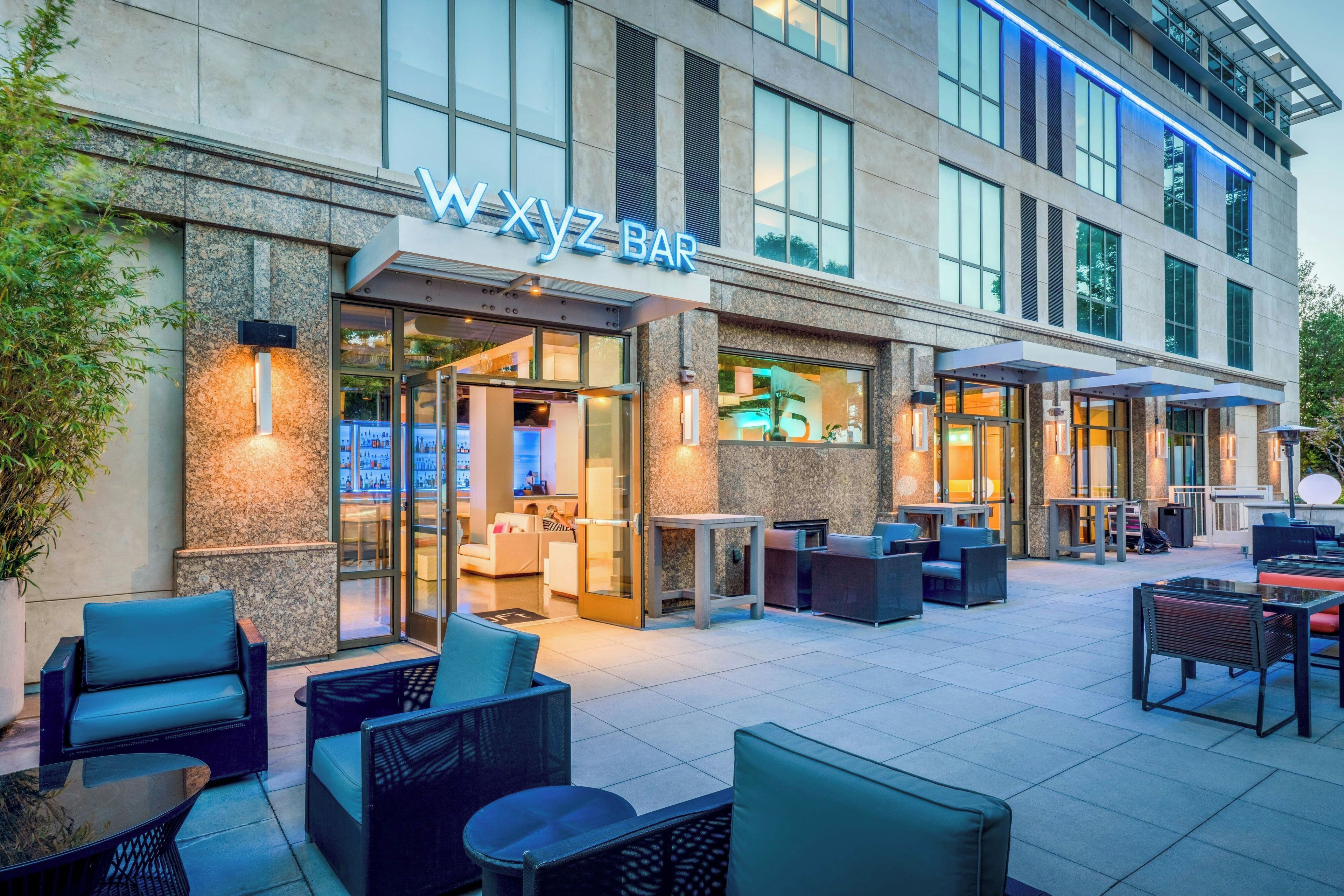 An outdoor seating area with tables and chairs, a bar entrance, and a building facade with a sign.