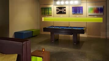 A pool table in a room with a curved wall, a green couch, and a small wooden table with a candle.