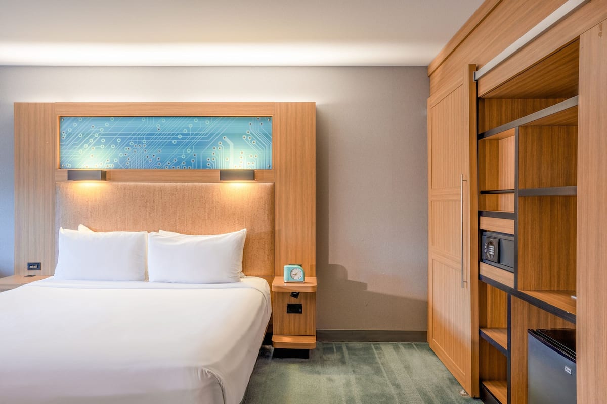 A hotel room with a bed, a nightstand with a clock, and a wooden wardrobe.