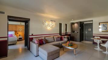 Una habitación de hotel moderna con sofá, reposapiés, mesa de centro y un área de comedor con sillas.