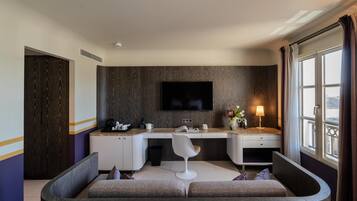 Habitación de hotel moderna con sofá curvo, escritorio con silla, televisor de pantalla plana y ventana con cortinas.