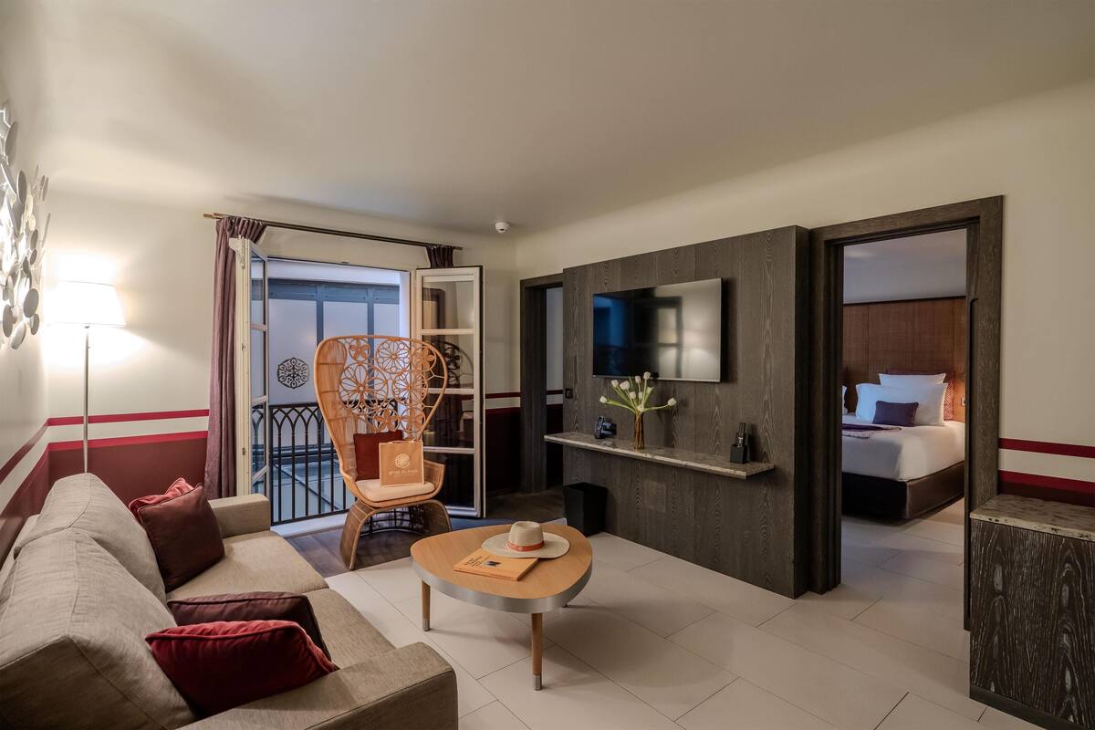 Une chambre d’hôtel avec un canapé, une petite table ronde, une chaise, un téléviseur fixé au mur et un lit dans la pièce adjacente.