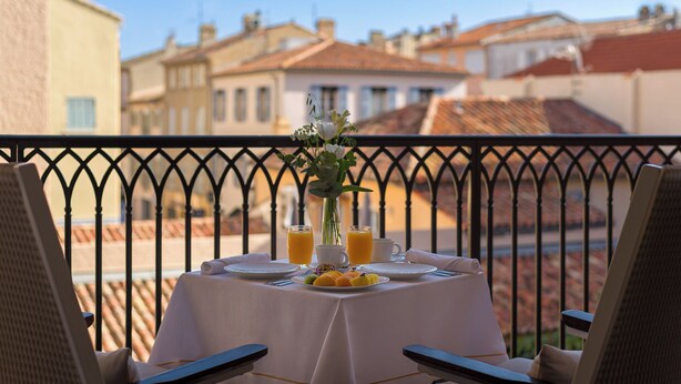 A balcony with a table set for breakfast, including plates, cutlery, and a vase of flowers.