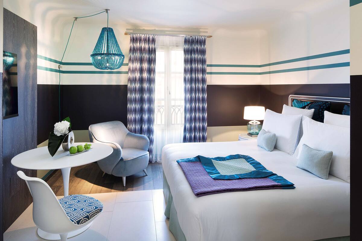 Une chambre d’hôtel moderne équipée d’un lit, d’un bureau, d’une chaise et d’un luminaire suspendu.