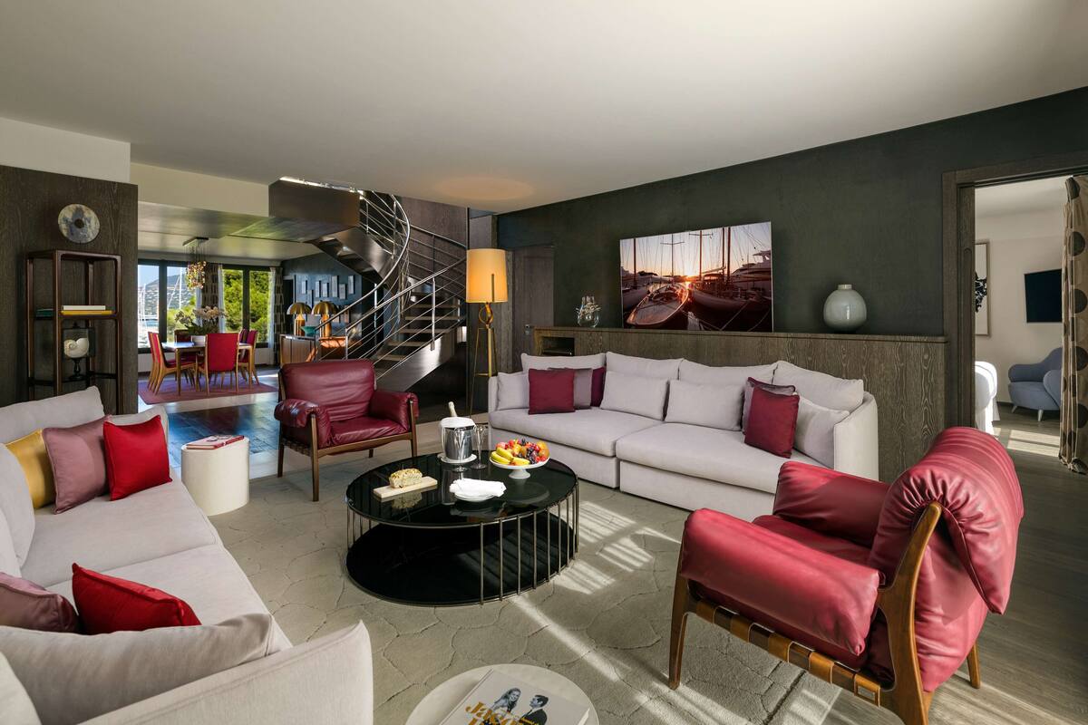 Un salon moderne avec un canapé blanc, des fauteuils rouges, une table basse en verre et un escalier.