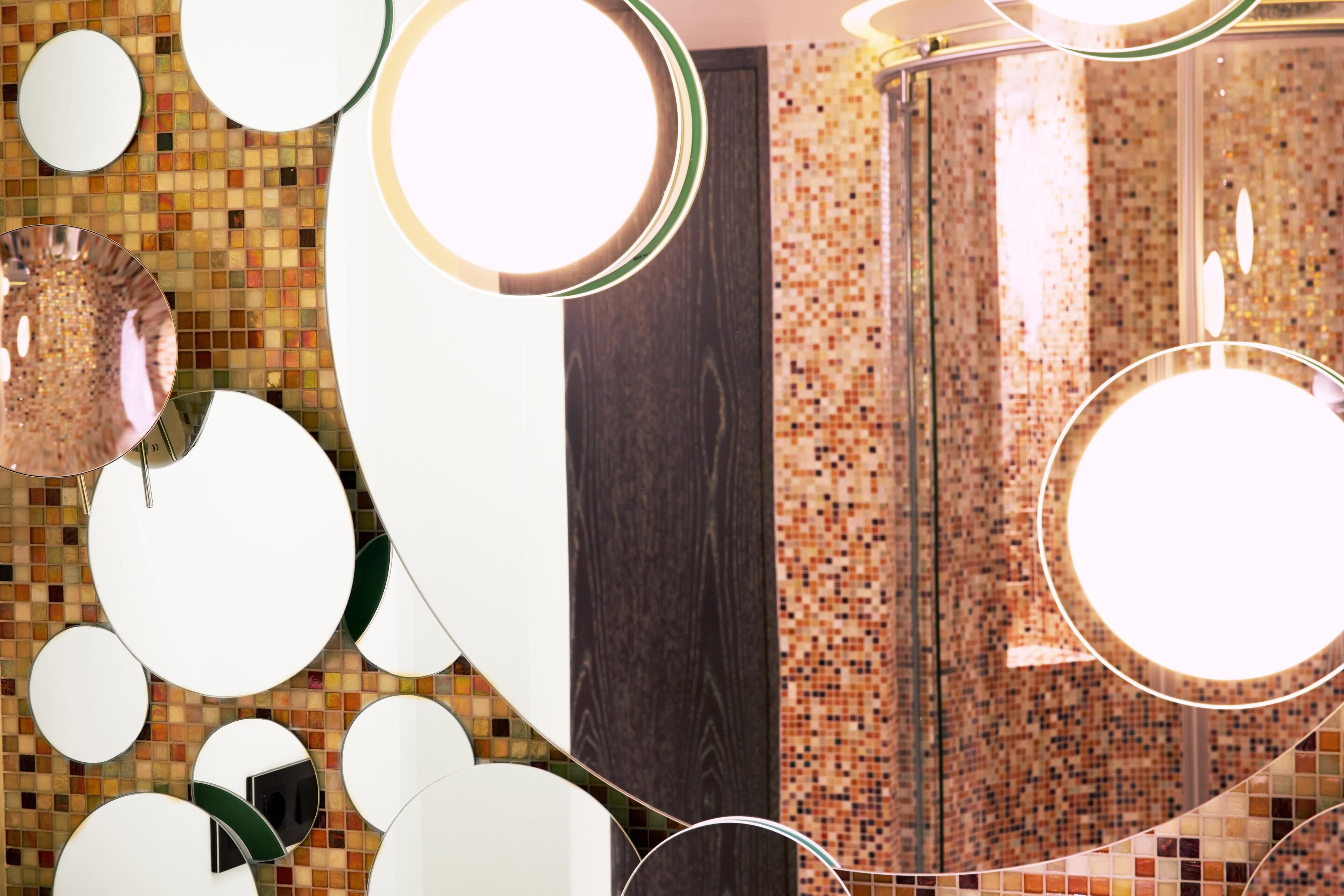 Une salle de bain avec plusieurs miroirs, un mur recouvert de mosaïques et un espace douche.