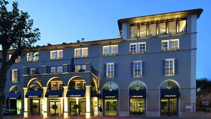 Un hotel de varios pisos con entradas en arco y balcones, con el nombre 'HOTEL DE PARIS' en la fachada.