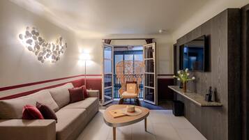 Una sala de estar moderna con un sofá, una mesa de centro, una lámpara de pared decorativa, un televisor y vistas a través de una puerta abierta.