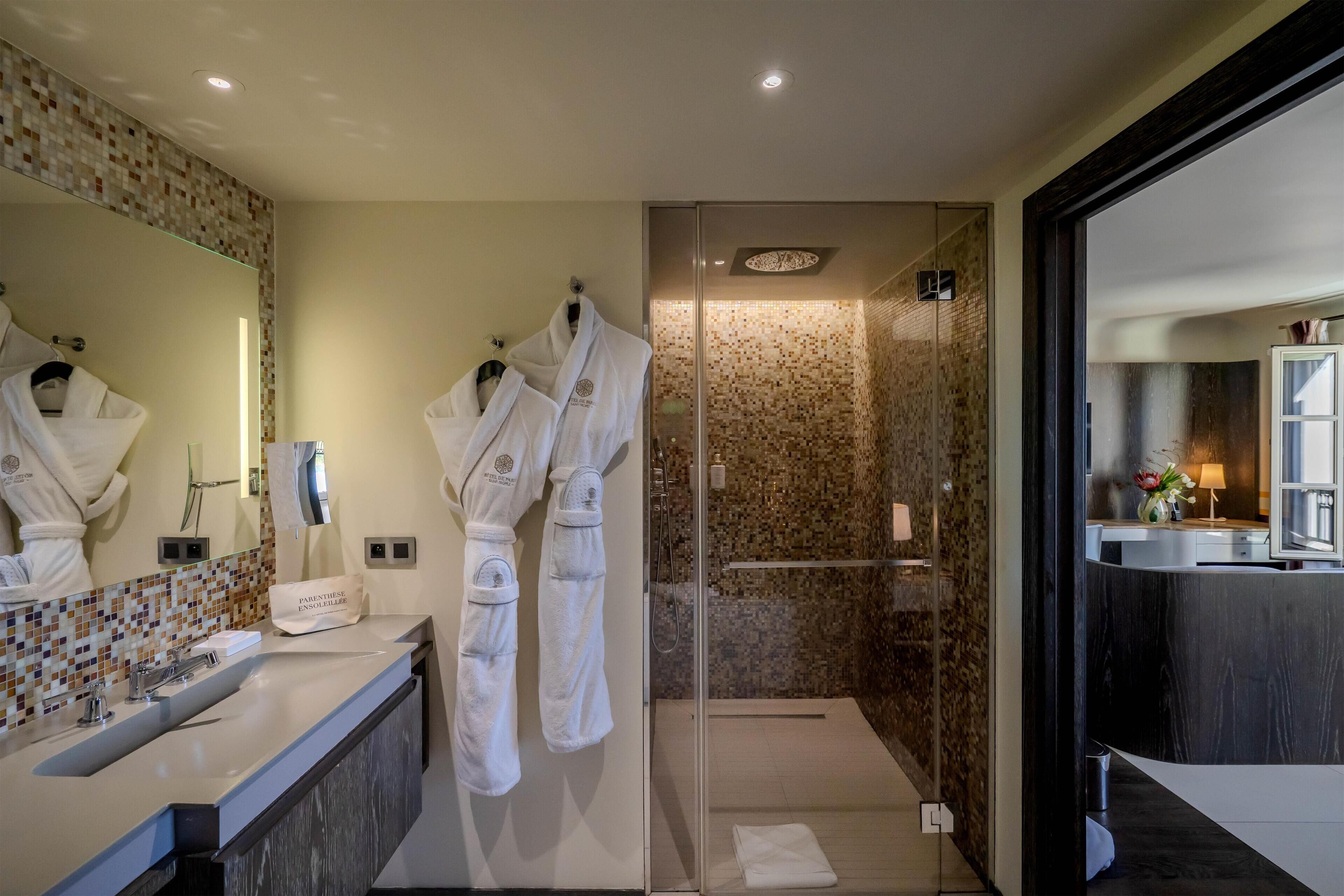 A modern bathroom with a large mirror, a sink, and two white robes hanging on hooks.