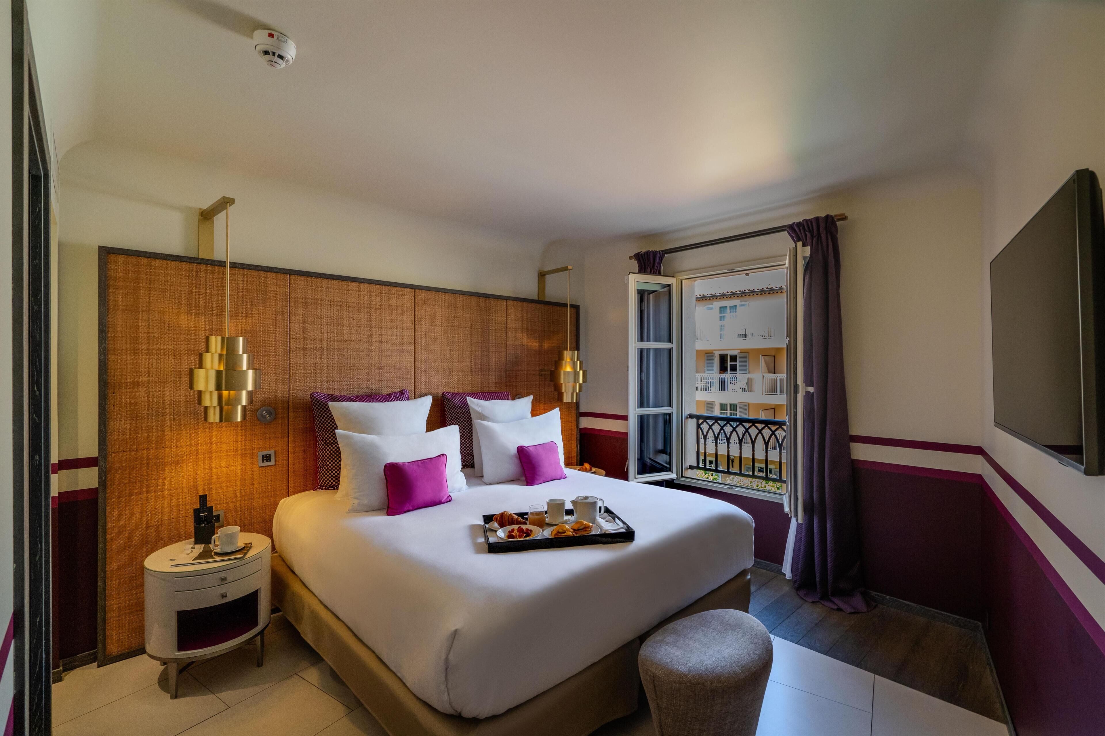Une chambre d’hôtel avec un grand lit, des tables de chevet, une fenêtre avec des rideaux et une vue sur un bâtiment à l’extérieur.
