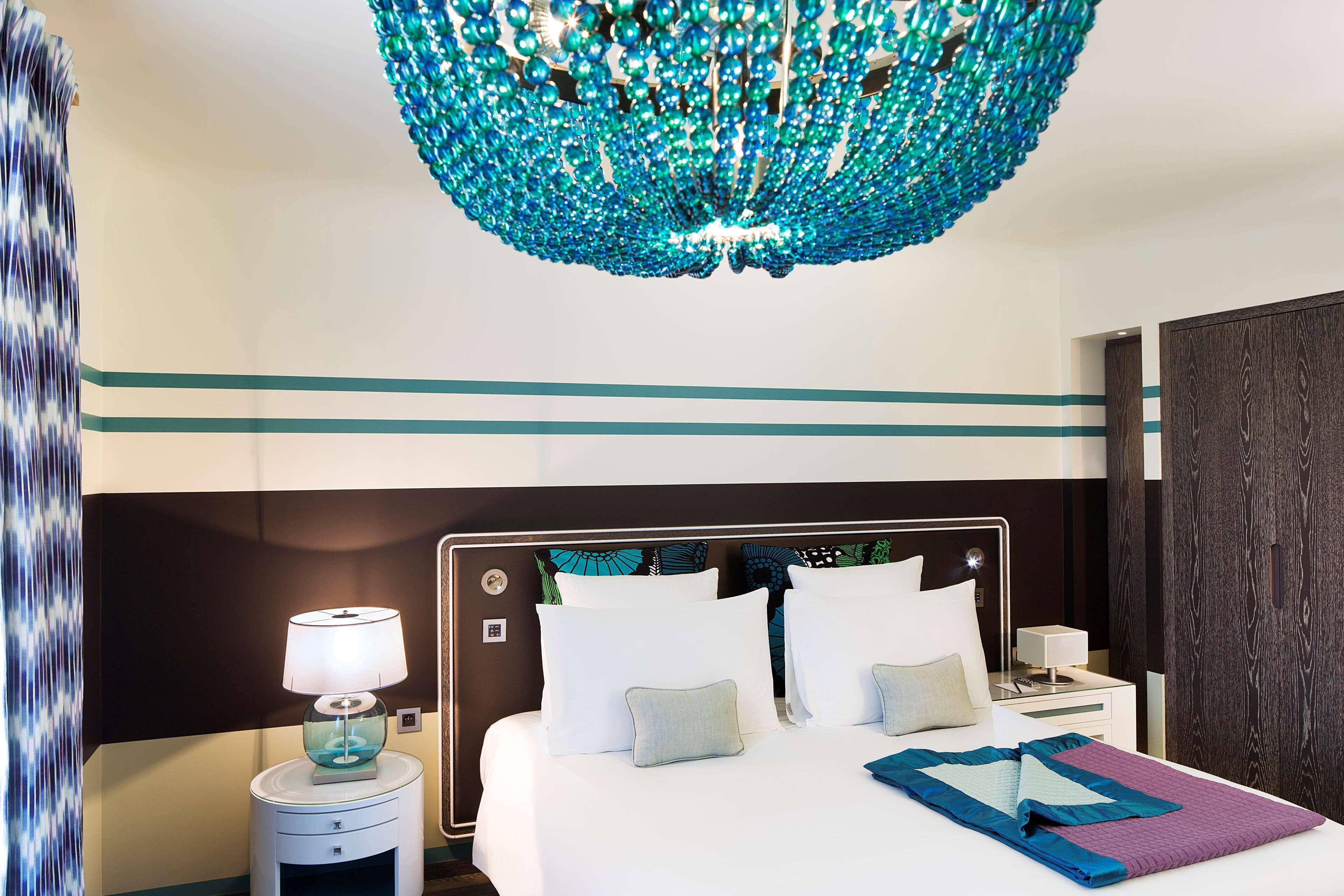 Une chambre d’hôtel avec un lit, une table de chevet, une lampe et un luminaire décoratif au plafond.