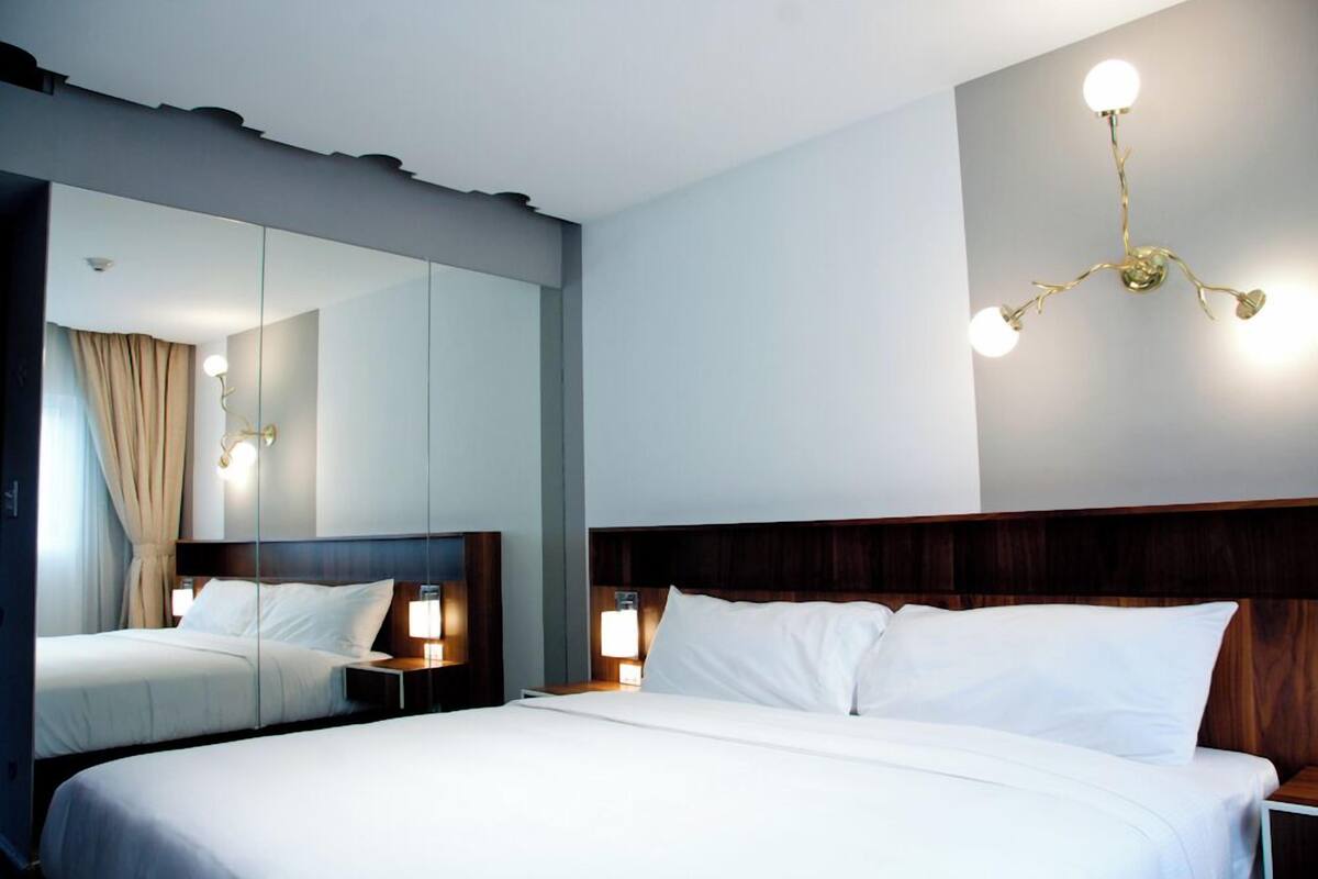 A hotel room with a large bed, a wooden headboard, bedside tables with lamps, and a modern chandelier.