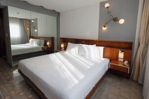 Una habitación de hotel con una cama grande, una mesita de noche con un teléfono, una mesita de noche con una lámpara y una lámpara de pared.