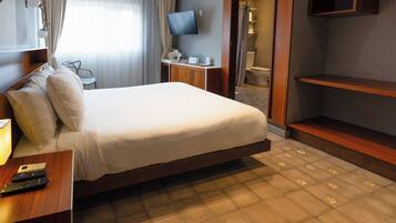 A hotel room with a bed, a desk with a lamp, a TV, and a bathroom visible through an open door.