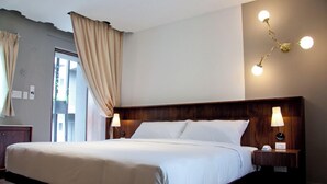 Habitación de hotel con una cama grande, cabecero de madera, dos lámparas de noche y un aplique de pared.