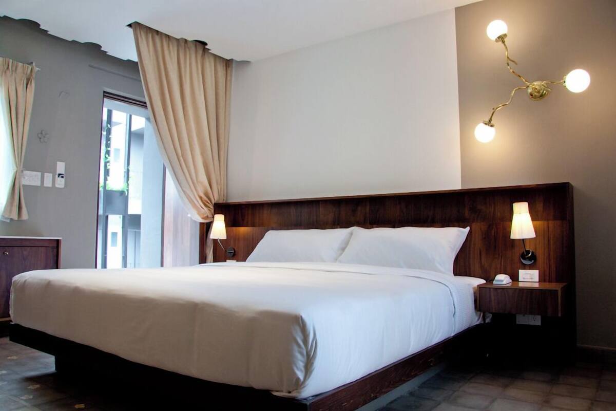 A hotel room with a large bed, wooden headboard, two bedside lamps, and a wall-mounted light fixture.