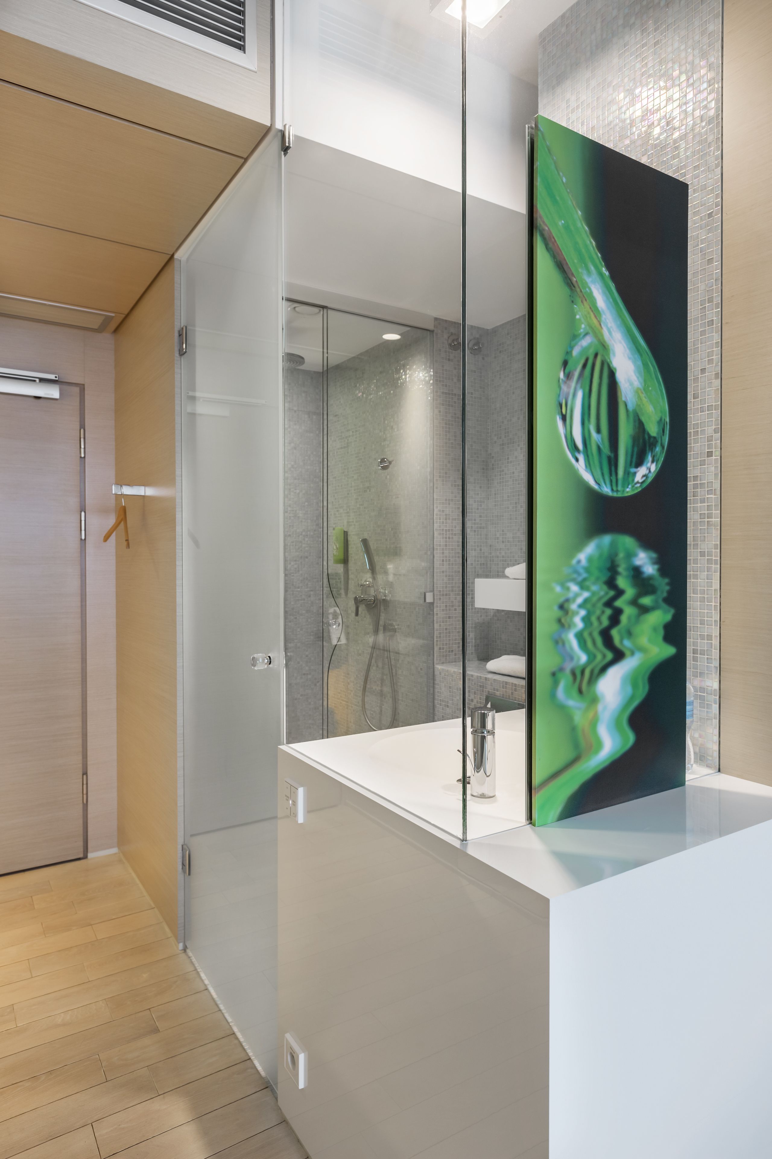 A modern bathroom with a glass shower enclosure, a white sink, and a large mirror with a green abstract design.