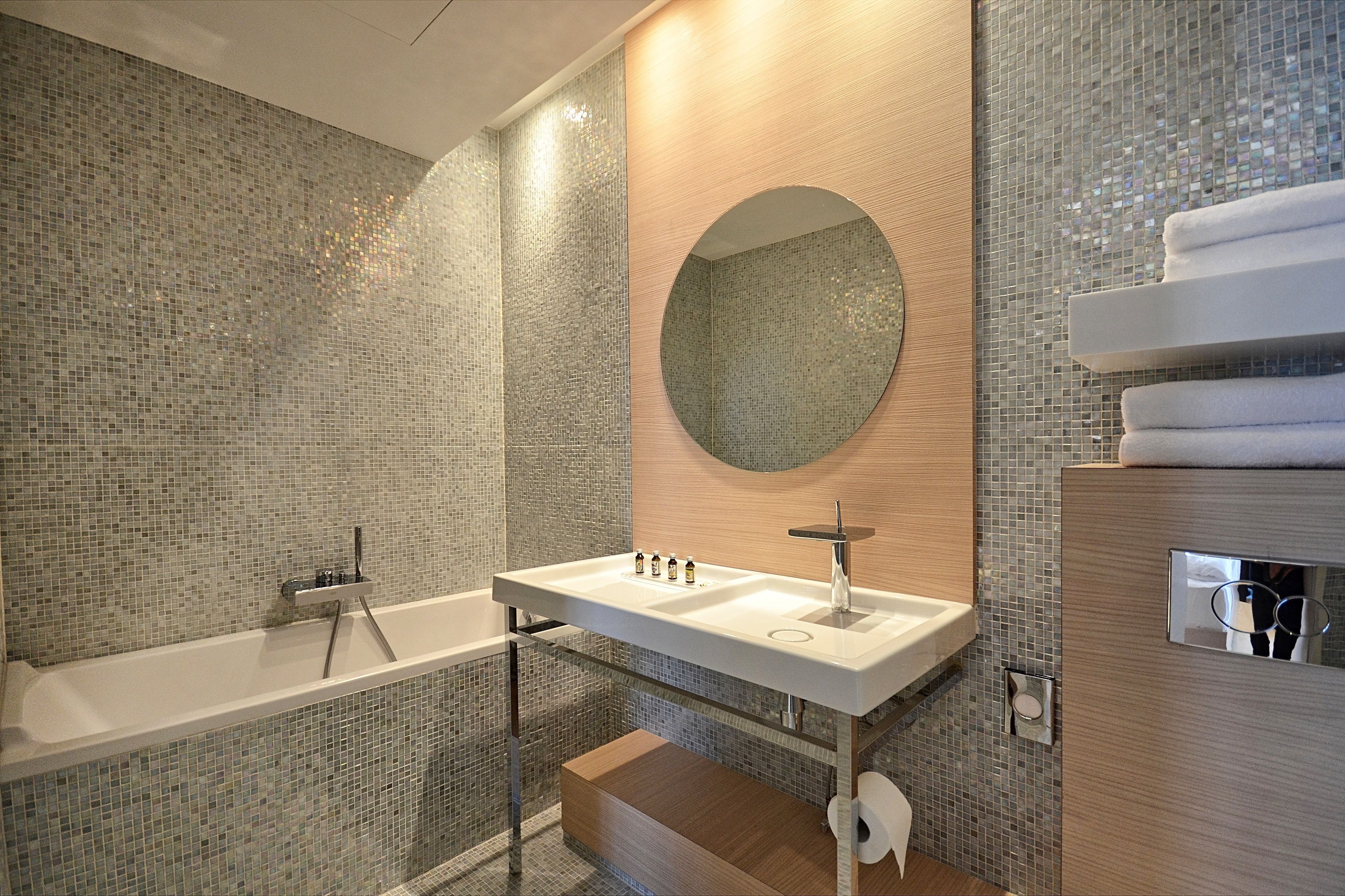 A modern bathroom with a glass-enclosed bathtub, a white sink with a mirror above it, and a wooden vanity with a towel rack.