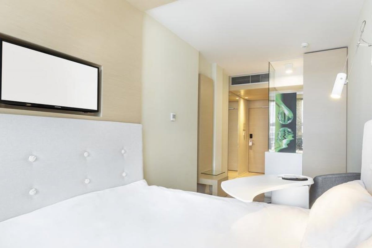 A modern hotel room with a large bed, a small desk, and a shower area.