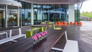 Un espacio exterior para comer con una larga mesa de madera, varias sillas y una fila de pequeños jarrones con flores rosas.