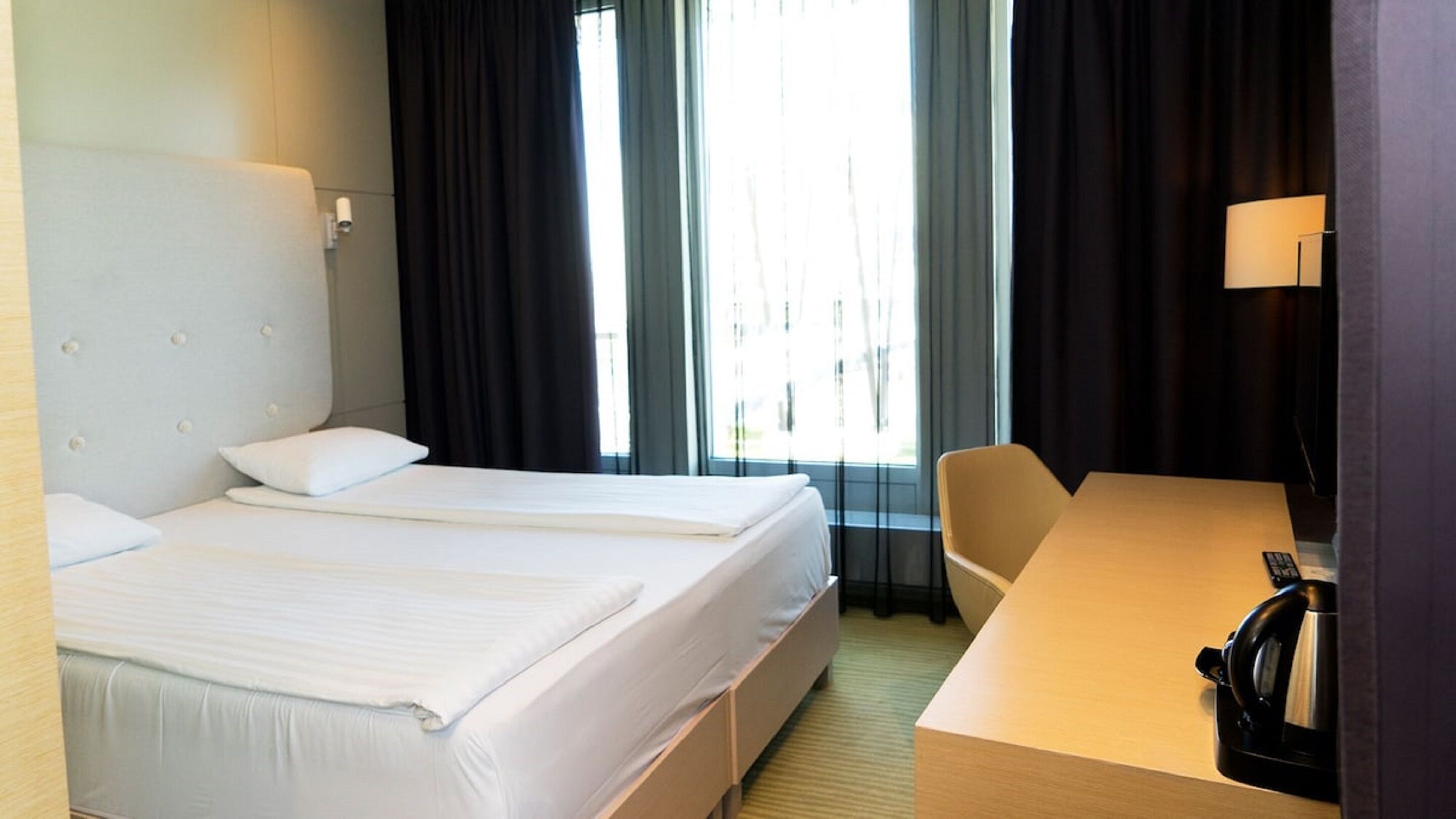 Ett hotellrum med två sängar, ett skrivbord, en stol och en vattenkokare.