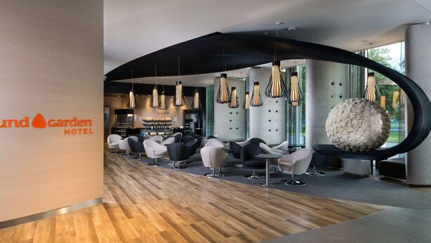 Un moderno vestíbulo de hotel con un mostrador de recepción curvo, zona de estar con sillas contemporáneas e iluminación colgante.