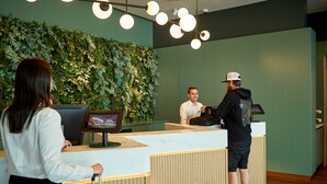 Una recepción con un mostrador de madera, una pantalla digital y una pared verde decorada con plantas.