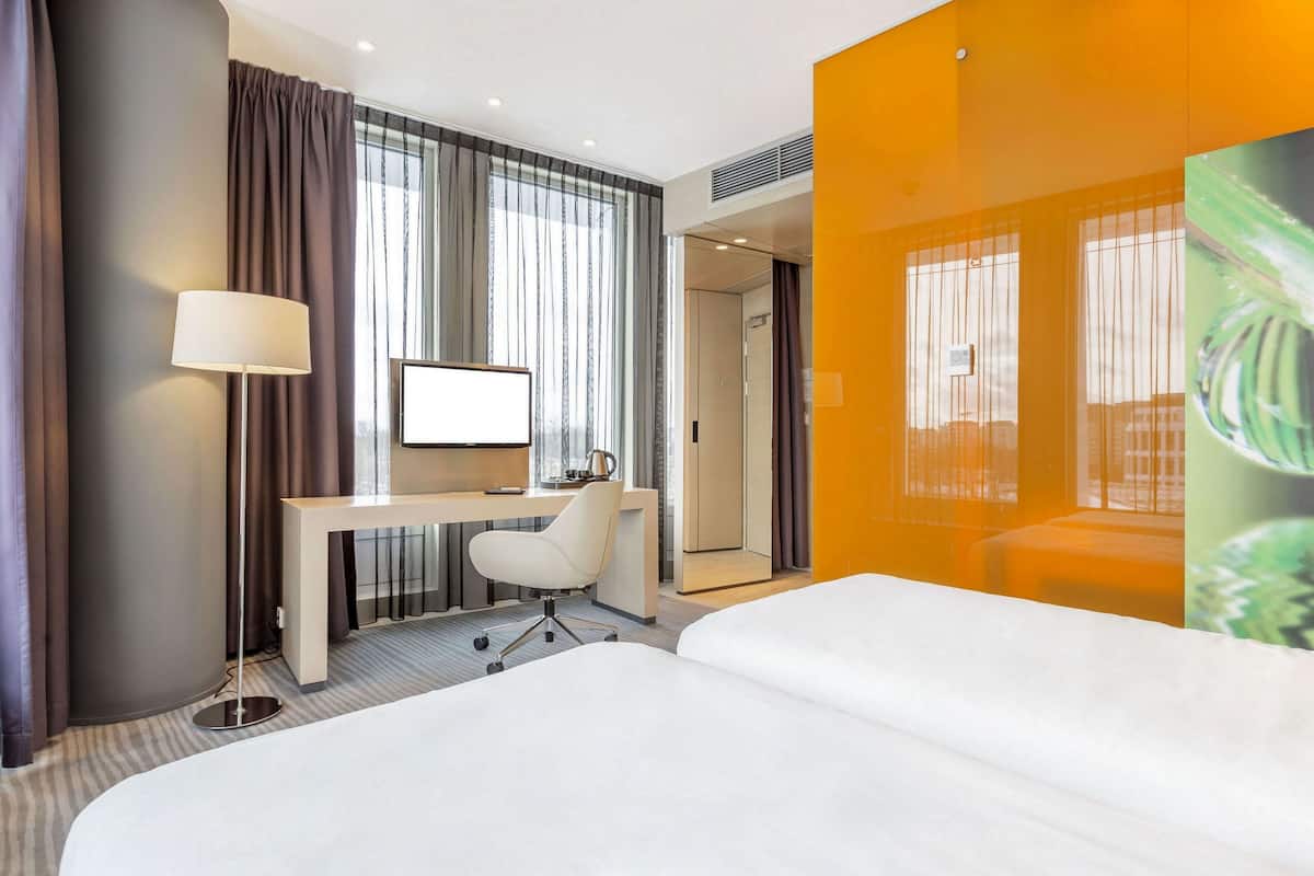 A hotel room with a bed, desk, chair, and a large window with curtains.