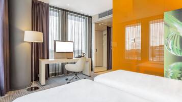 A hotel room with a bed, desk, chair, and a large window with curtains.