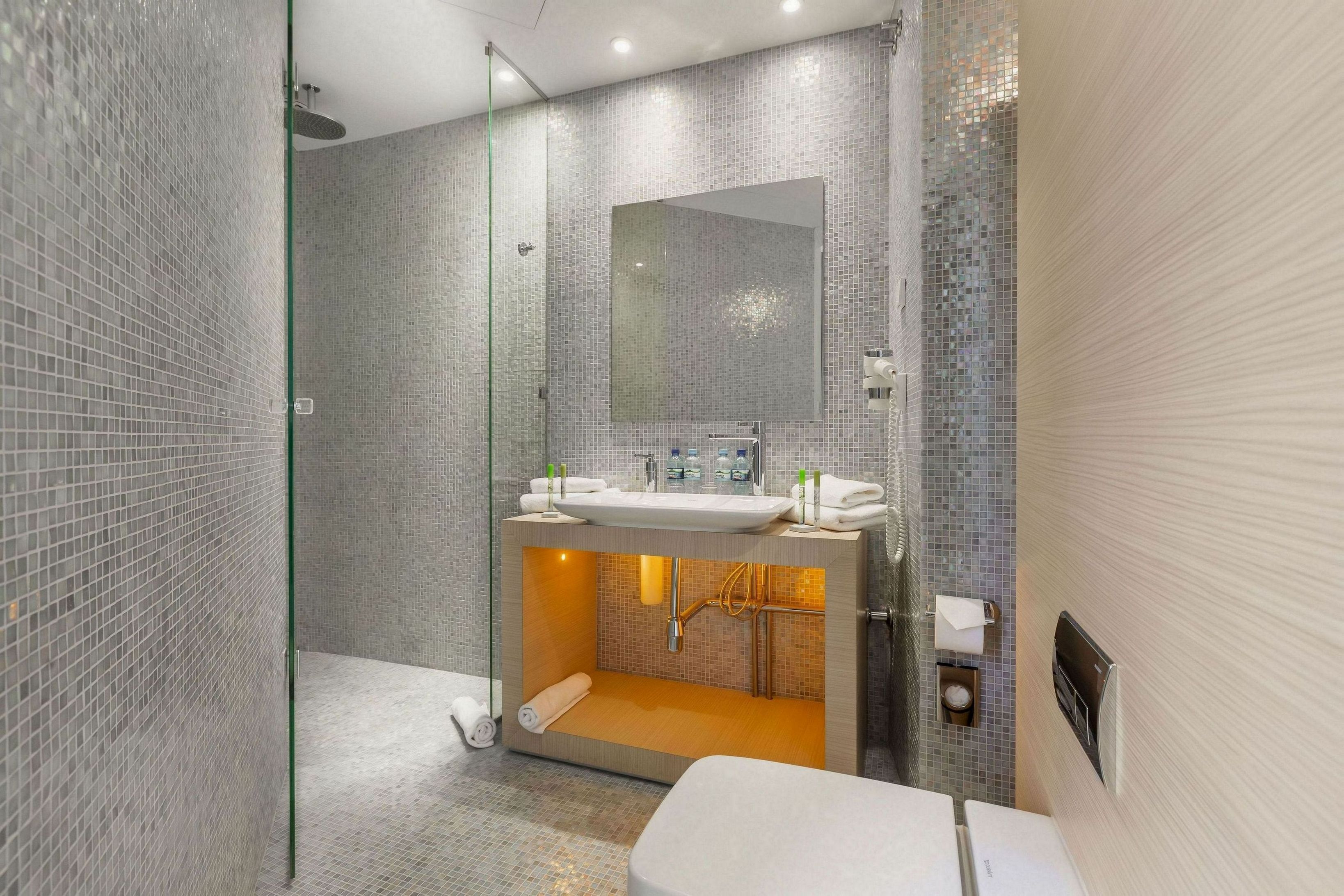 A modern bathroom with a glass-enclosed shower, a large mirror, and a sink with a towel rack.