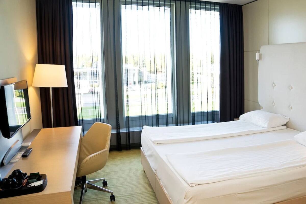 A hotel room with a bed, a desk with a lamp, a chair, and a TV.