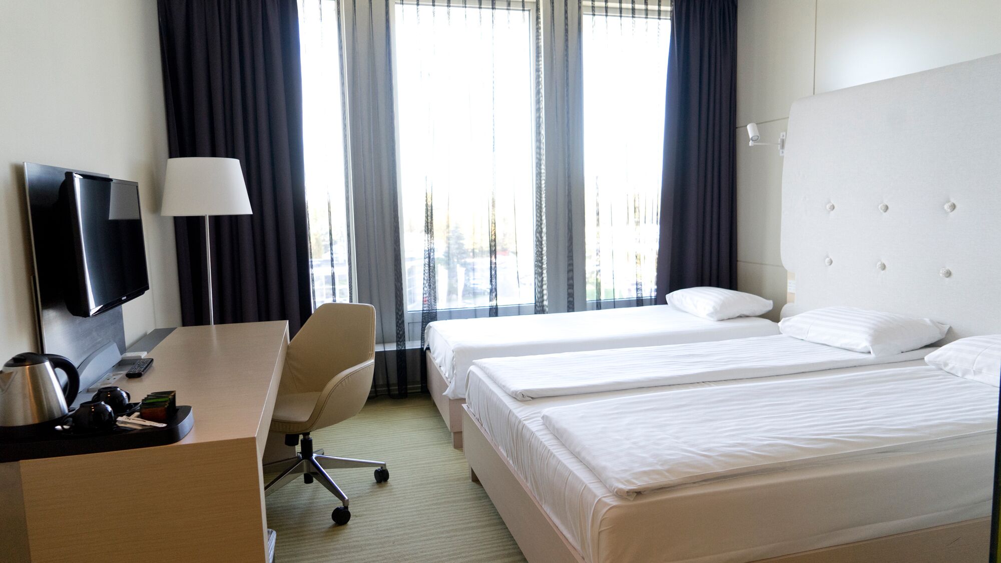 Habitación de hotel con dos camas, un escritorio con lámpara, un televisor y una silla.
