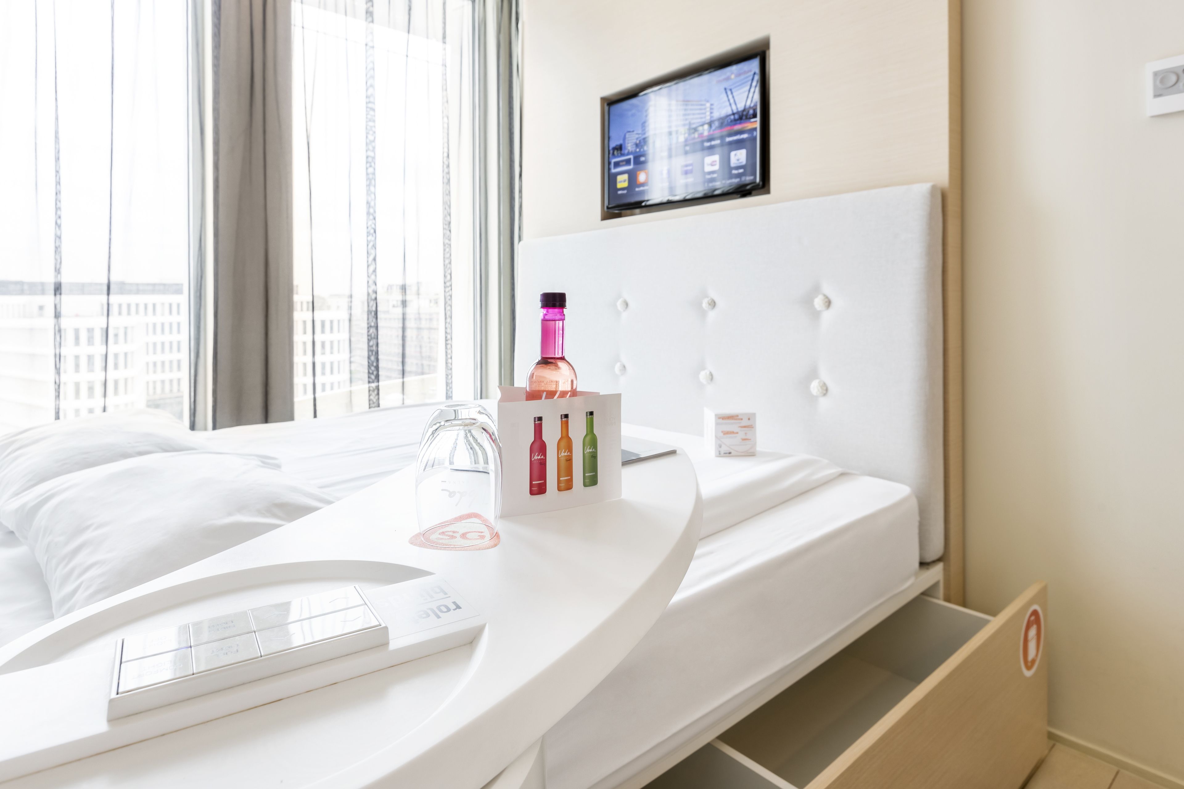 Habitación de hotel moderna con una cama curvada, una pantalla digital en la pared y vistas de la ciudad.